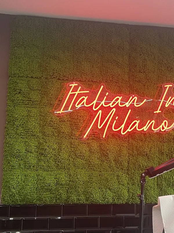 Insegna al neon Italian Ink Milano su parete verde